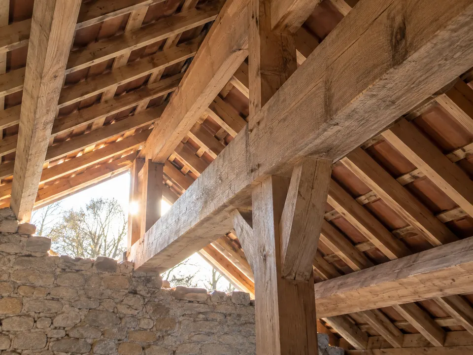 Charpente traditionnelle en bois vue en contre-plongée : pannes, chevrons et arêtiers assemblés